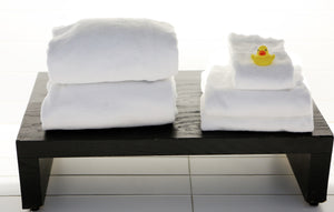 Four folded white towels on a table with a rubber duck on top